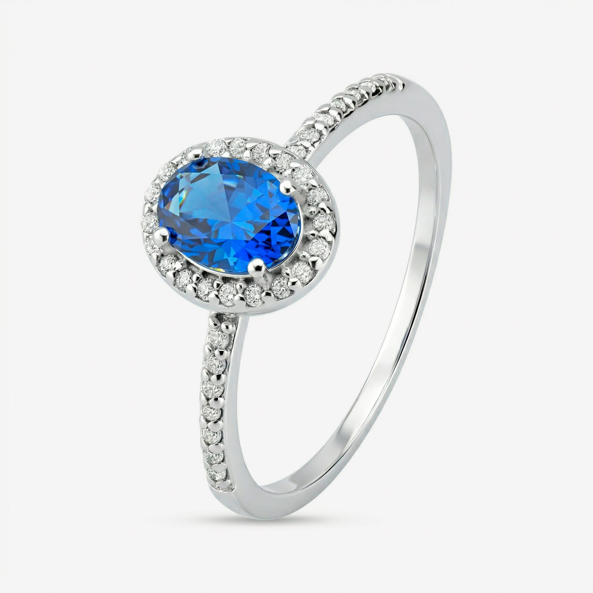 Anel Ivel em prata 925 com zircônia central oval azul, halo de zircônias brancas e fileira cravejada no aro até a metade da banda, vista lateral