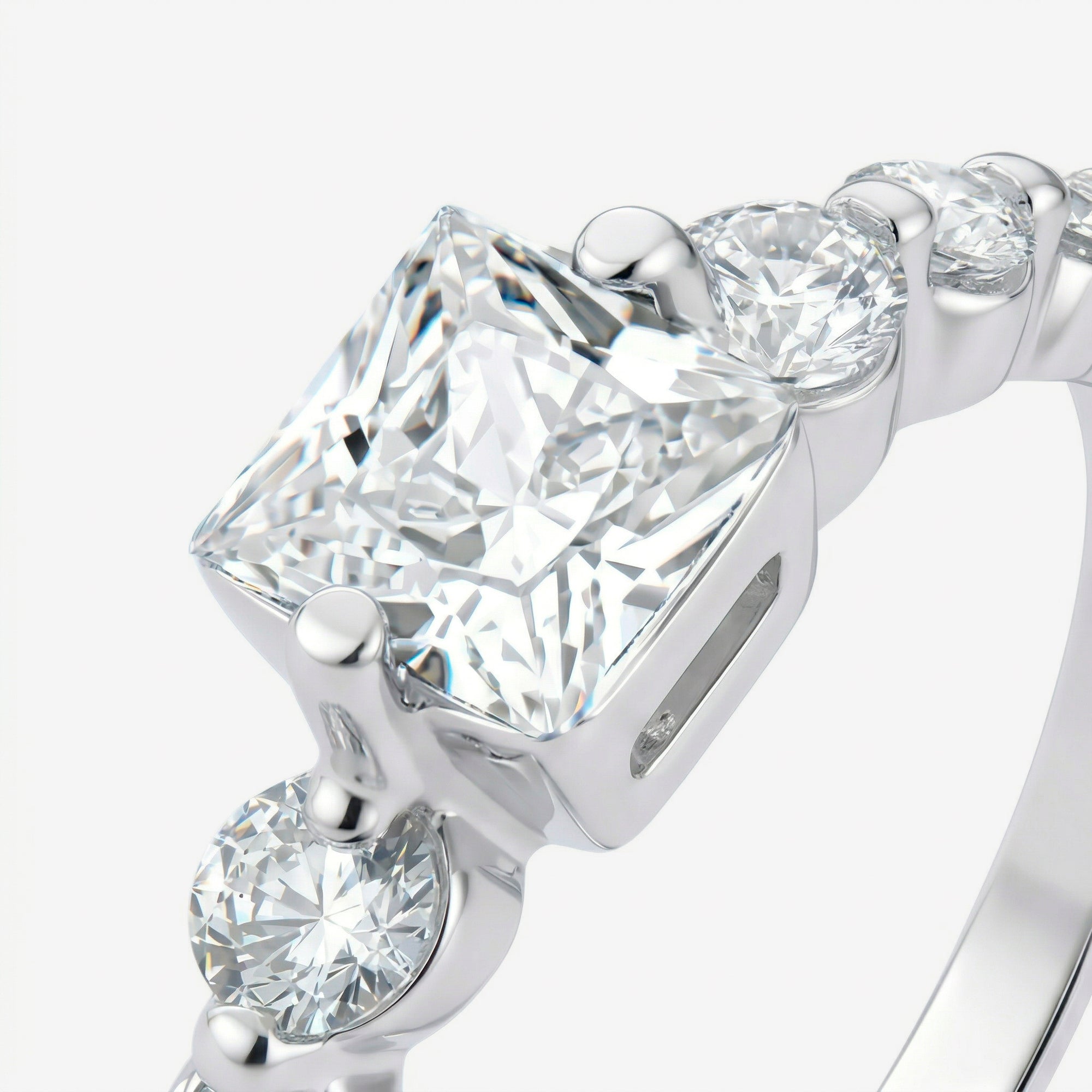Detalhe da zircônia central de corte princess com quatro garras e zircônias redondas no aro do Anel Kael em prata 925