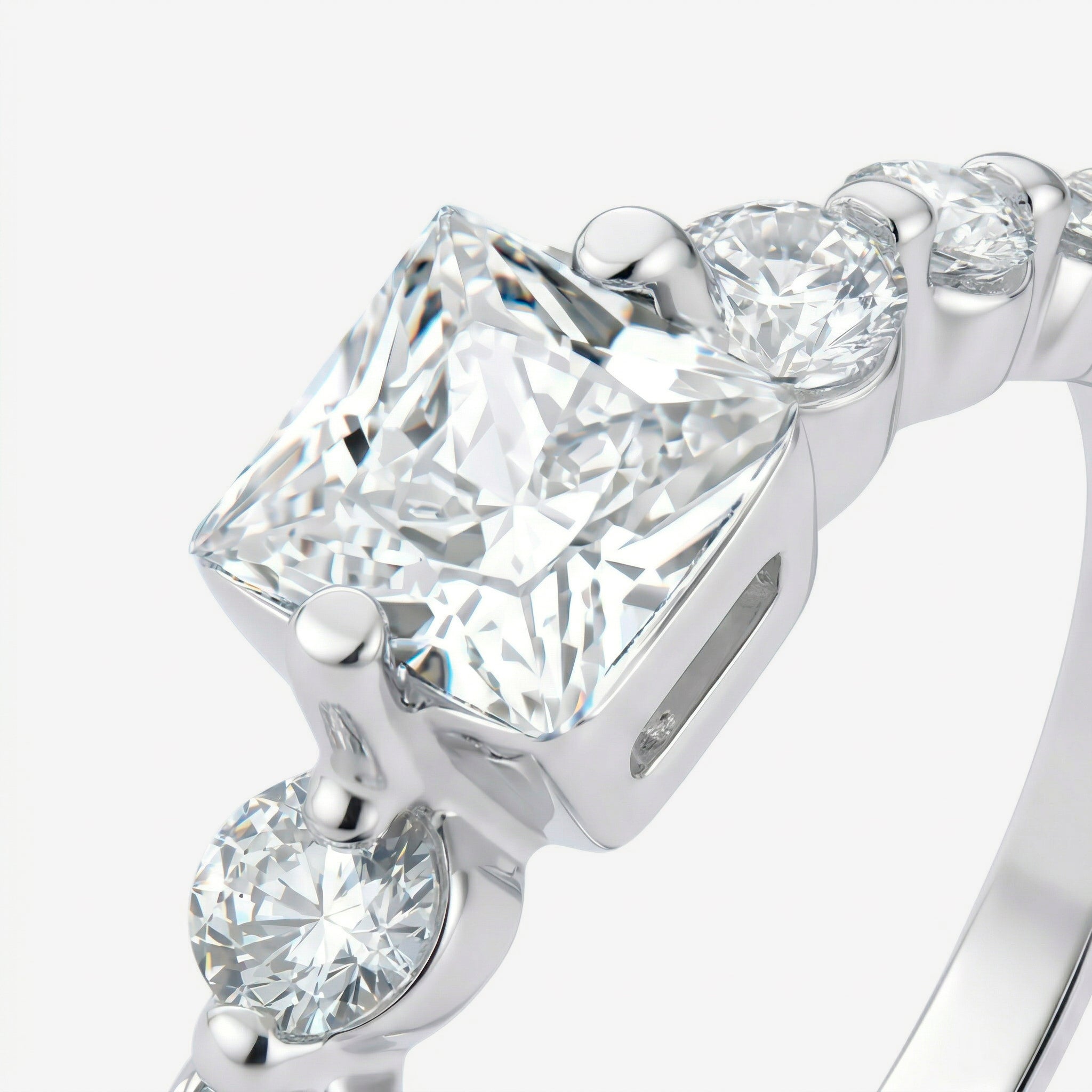 Detalhe da zircônia central de corte princess com quatro garras e zircônias redondas no aro do Anel Kael em prata 925
