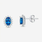 Par de brincos Avel em prata 925 com zircônia oval azul intenso em quatro garras e halo de zircônias brancas, vista frontal e lateral com fecho tarracha
